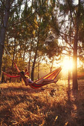 Woman lying in hammock at sunny woods - ADSF00172