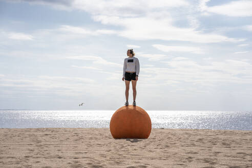 Junge Frau steht auf orangefarbenem Stein am Strand - VPIF02580