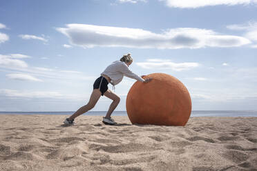 Junge Frau rollt orangefarbenen Stein am Strand - VPIF02583