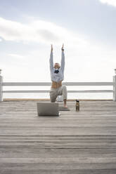 Young athletic woman using laptop for workout on jetty - VPIF02589