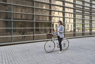 Nachdenkliche Geschäftsfrau steht mit Fahrrad auf der Straße in der Stadt - VEGF02455