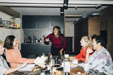 Cheerful female entrepreneur gesturing while coworkers sitting at table in creative office - MASF19340