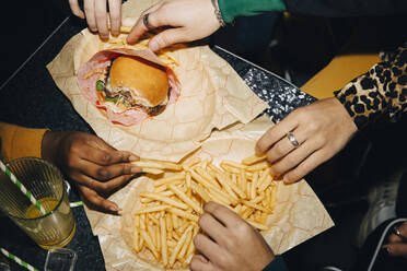High angle view of friends eating burger and french fries at table in cafe - MASF19354