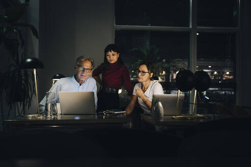 Senior businessman planning strategy with female colleagues at coworking space in dark - MASF19369