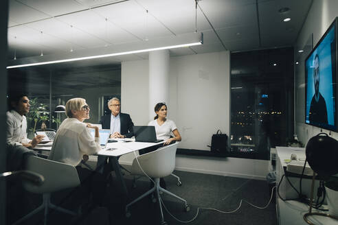 Colleagues looking at businessman during video conference meeting at night in office - MASF19380