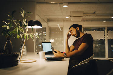 Exhausted businessman with head in hand working late at creative office - MASF19411