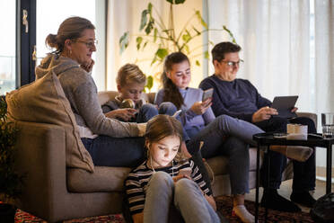 Eltern, die mit ihren Kindern zusammensitzen und drahtlose Technologien im Wohnzimmer eines modernen Hauses nutzen - MASF19428