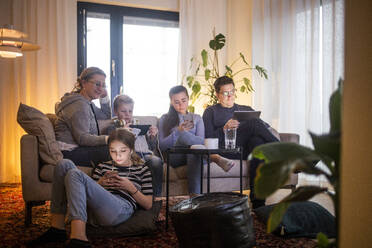 Family using wireless technologies in living room while relaxing on sofa at modern home - MASF19429