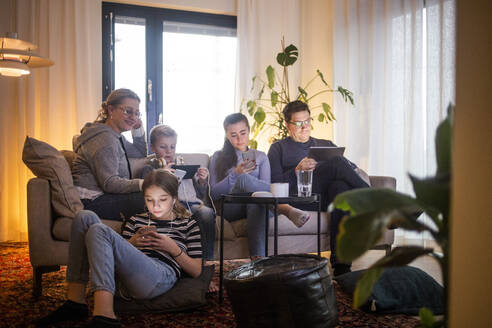 Familie nutzt drahtlose Technologien im Wohnzimmer, während sie sich auf dem Sofa in einem modernen Haus entspannt - MASF19429