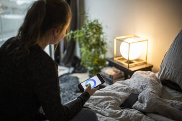 Teenager-Mädchen, das eine Smartphone-App benutzt, während es die Beleuchtung im Schlafzimmer im Smart Home einstellt - MASF19438