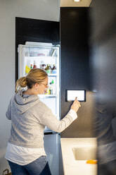 Frau benutzt digitales Tablet am intelligenten Kühlschrank in einem modernen Haus - MASF19447