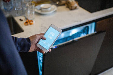 Ausgeschnittenes Bild eines Mannes, der eine mobile App für einen Geschirrspüler im Smart Home nutzt - MASF19448