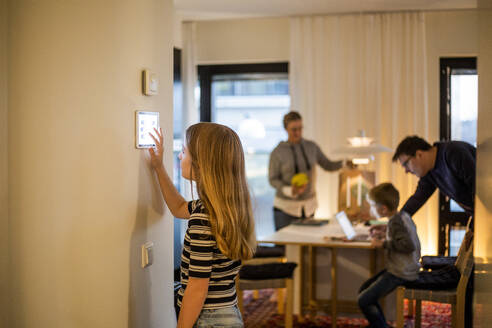 Mädchen benutzt digitales Tablet an der Wand mit Familie im Hintergrund im Smart Home - MASF19454