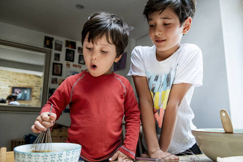 Two boys with black hair sitting at a kitchen table, baking chocolate cake. - CUF55684