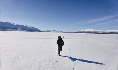 Rückansicht von zwei Jungen, die über einen zugefrorenen See in Vasterbottens Lan, Schweden, laufen. - CUF55711