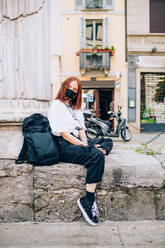 Young woman wearing face mask during Corona virus, sitting outdoors, looking at camera. - CUF55749