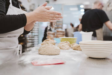 Bäckerin streut Mehl auf den Brotteig auf dem Küchentisch in einer Bäckerei - EBBF00365