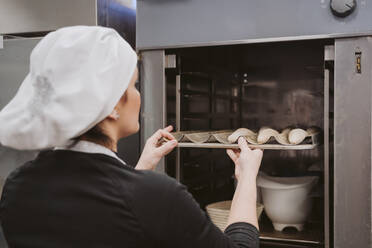 Bäckerin beim Einschieben der Backform in den Ofen in einer Bäckerei - EBBF00371