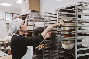 Bäckerin legt Brötchenschale in die Ablage eines Bäckereiwagens ein - EBBF00381