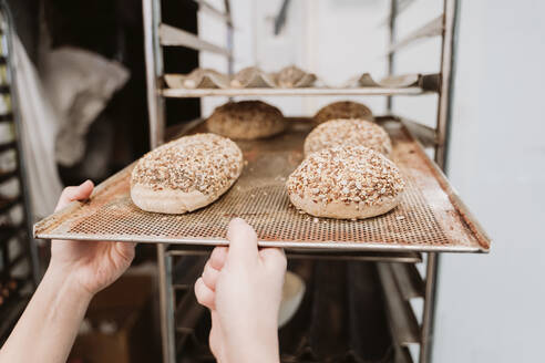 Baker inserting bun tray in shelf of trolley at bakery - EBBF00382