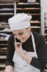 Glückliche Bäckerin benutzt Smartphone in Großküche - EBBF00387