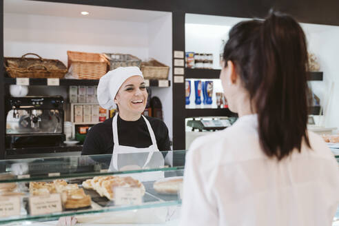 Glückliche Bäckerin, die einen Kunden in einer Bäckerei bedient - EBBF00401
