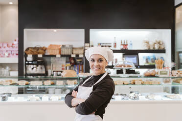 Confident female baker standing arms crossed at bakery - EBBF00409