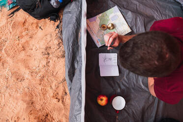 Ein junger Mann liegt im Zelt und zeichnet in einem Skizzenbuch beim Camping in der Wüste - ADSF00230