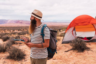 Man holding map and retro compass while standing on blurred background of majestic desert - ADSF00232