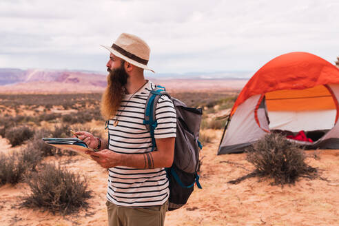 Ein Mann hält eine Landkarte und einen Retro-Kompass in der Hand, während er vor einem unscharfen Hintergrund einer majestätischen Wüste steht - ADSF00232