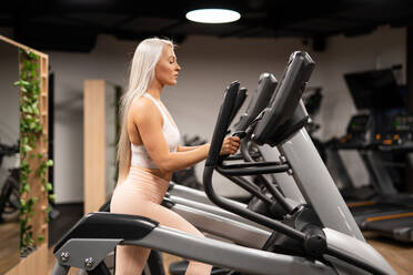 Seitenansicht einer schönen Frau in Sportkleidung bei einer Übung auf dem Stepper im Fitnessstudio - ADSF00256