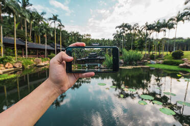 Crop hand using smartphone and taking photo of oriental building on tropical lake of Qingxiu Mountain, China - ADSF00267