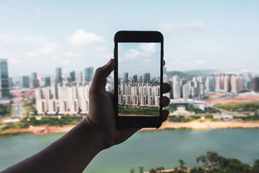 Crop Hand hält Smartphone und nimmt Bild der modernen Stadt Nanning aus der Höhe, China - ADSF00270