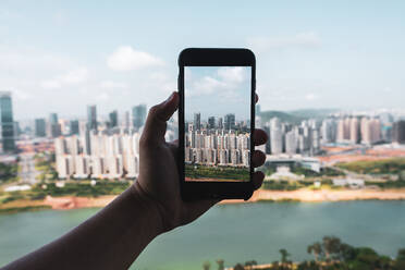 Crop hand holding smartphone and taking picture of contemporary city of Nanning from height, China - ADSF00270