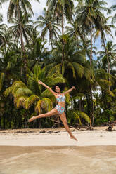 Young lady standing on sand beach with tropical forest near water - ADSF00297