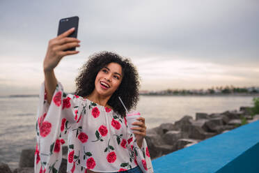 Frau mit Telefon und Getränk macht Selfie am Wasser - ADSF00305
