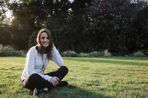 Glückliche erwachsene Frau sitzt im Gras im Park - DCRF00355