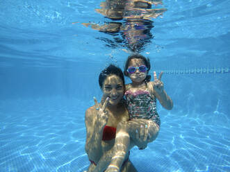 Mutter und Tochter gestikulieren das Friedenszeichen im Schwimmbad - EGAF00427
