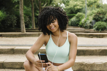 Sportliche junge Frau benutzt Smartphone im Park - XLGF00331