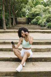 Sportliche junge Frau benutzt Smartphone im Park - XLGF00332