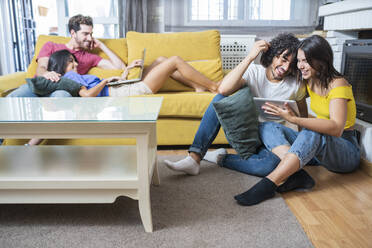 Glückliche junge Paare, die im Wohnzimmer sitzend Technologien nutzen - JSMF01598