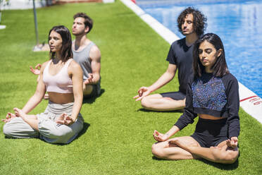 Junge multiethnische Freunde beim Meditieren und Yoga auf dem Rasen im Hinterhof bei sonnigem Wetter - JSMF01620