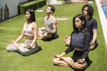 Junge Mala und weibliche Freunde meditieren während sie Yoga auf dem Rasen im Hinterhof bei sonnigem Wetter üben - JSMF01621