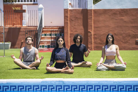 Young mala and female friends meditating while practicing yoga on grass at back yard against house during sunny stock photo