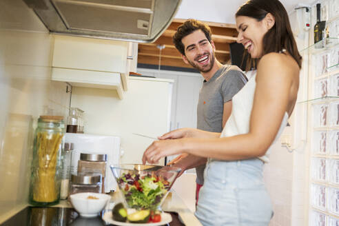 Fröhliches junges Paar bei der Zubereitung einer gemeinsamen Mahlzeit in der Küche zu Hause - JSMF01625