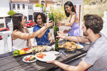 Glückliche junge Freunde stoßen mit Bierflaschen an, während sie auf der Terrasse des Gebäudes brunchen - JSMF01627