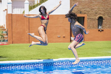 Happy young couple diving into swimming pool at back yard on sunny day - JSMF01645