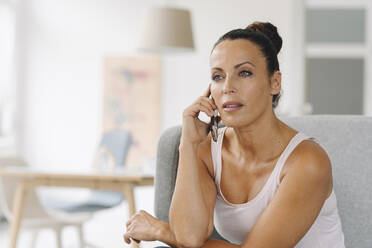 Close-up of businesswoman talking over smart phone while sitting on sofa at home office - JOSEF01258