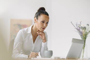 Businesswoman looking at laptop while working on desk in home office - JOSEF01262