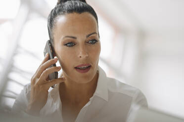 Close-up of businesswoman talking over smart phone in home office - JOSEF01274